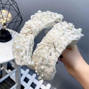 Close-up of white lace headband with 3D floral texture and hand-stitched faux pearls