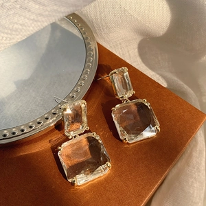 Detail of transparent geometric crystal drop earrings with gold claws on leather