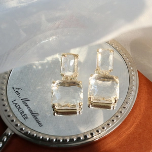 Close-up of geometric square crystal earrings with gold prong setting on a reflective mirror