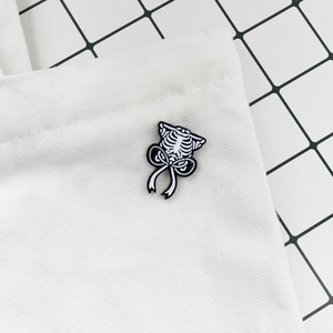 Close-up of a rib cage enamel pin with a black bow on a white canvas bag strap