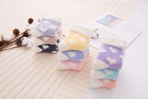 Folded colorful heart pattern coral fleece socks displayed on a soft knitted blanket