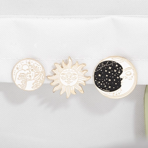 Close-up of enamel pins featuring sun, moon, and mountain designs on white fabric