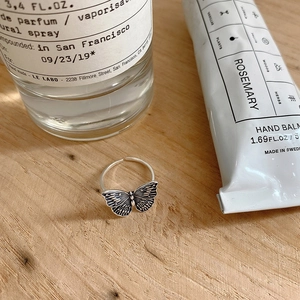 Detail of vintage silver butterfly open ring displayed on light wood surface with props