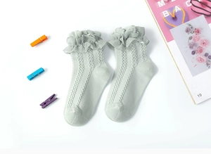 Close-up of light green knit baby socks featuring delicate white lace ruffle trim edges