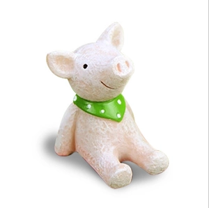 Close-up of cute pink resin pig figurine with a green polka dot scarf on white background