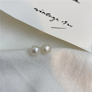 Close-up of small freshwater pearl stud earrings on white linen fabric with vintage card