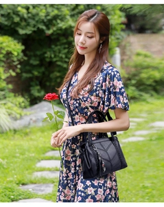 Black leather tote bag with V-shaped stitching and tassel detail in outdoor garden setting