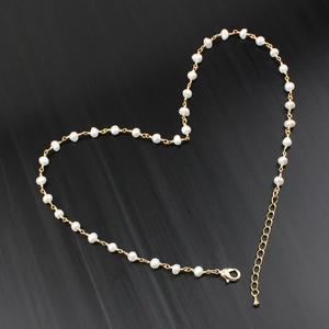 Elegant heart-shaped layout of a small white pearl necklace with gold lobster clasp