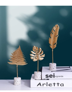 Close-up of golden metal monstera and fern leaf ornaments with terrazzo bases