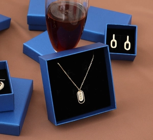 Detail of luxury peacock blue jewelry boxes with gold Roman numeral necklace and earrings