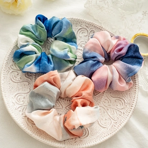 Three tie-dye elastic scrunchies in blue, pink and orange silk on a vintage white plate