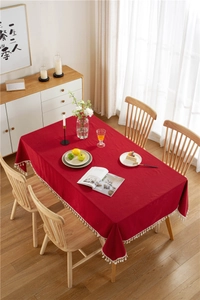 Detail of dark red cotton tablecloth edge featuring elegant white fringe tassels on wood table