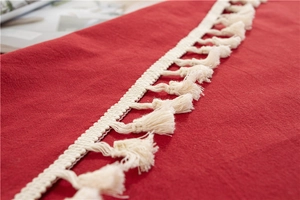 Macro view of red washed cotton tablecloth featuring elegant beige fringe tassels