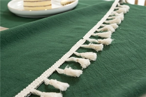 Close-up of dark green cotton tablecloth texture with elegant cream fringe tassels