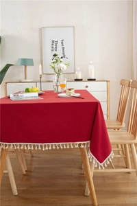 Close-up of red cotton tablecloth with white tassels and festive dining table decor