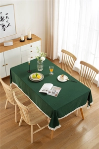 Detail of dark green cotton tablecloth with white decorative tassels on a wooden table