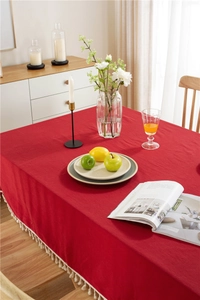 Detail shot of red cotton tablecloth with beige tassel fringe on wooden dining table