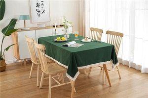 Close-up of green cotton tablecloth featuring decorative cream tassel fringes on wood table