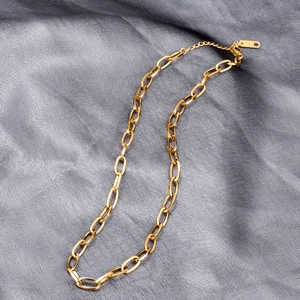 Flat lay of a gold chunky oval link chain necklace on textured grey fabric background