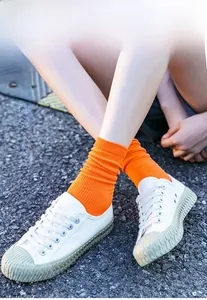 Detail of bright orange ribbed socks paired with white canvas sneakers on asphalt