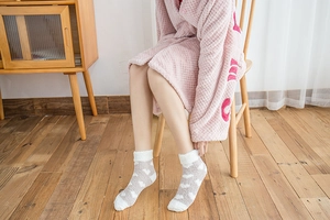 Detail view of plush coral fleece heart socks worn on feet over a wooden floor