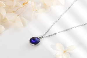 Detailed view of silver necklace with round dark blue crystal pendant on white background