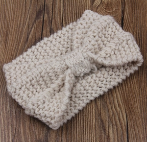 Detail of chunky knit cream headband with large bow texture on wood background