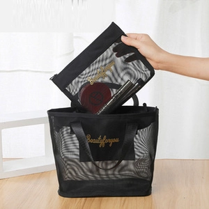 Macro detail of black mesh cosmetic bags with gold embroidery logo in hand