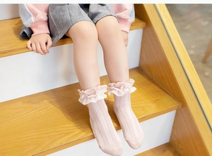 Detailed view of pink lace ruffle socks on a child model sitting on wooden stairs