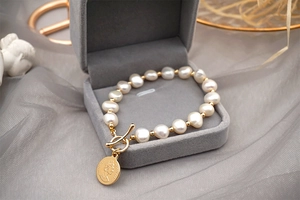 Detailed macro view of baroque pearl bracelet with gold coin charm and toggle clasp