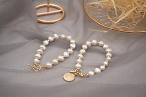 Close-up of freshwater pearl bracelets with golden T-bar clasp and vintage coin charm