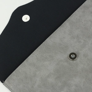 Detail of silver magnetic snap closure on a black and grey faux suede envelope brush bag