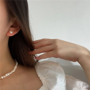 Close-up of minimalist white freshwater pearl stud earrings and necklace worn by a model