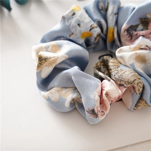 Close-up of light blue floral satin scrunchie with soft pastel blossom patterns