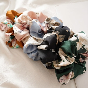 Flat lay of satin floral scrunchies in assorted colors on a white linen surface