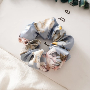 Detailed shot of light blue floral satin scrunchie with silky texture and soft print