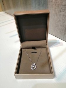 Close-up of a silver necklace with a round diamond pendant in a dark brown jewelry gift box