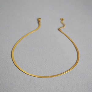 Detail of a thin gold-plated flat snake chain necklace with an adjustable lobster clasp