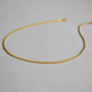 Macro detail of a golden snake bone chain necklace on a textured grey background