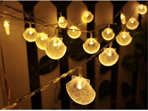 Close-up of warm yellow seashell LED string lights on a garden fence at night
