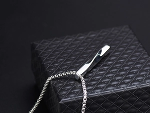 Close-up of twisted silver bar pendant on a textured black gift box with metallic shine