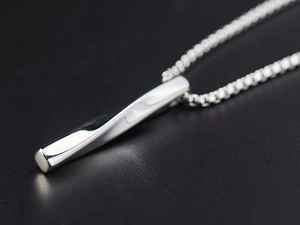 Macro shot of a twisted bar pendant and silver box chain on a black background