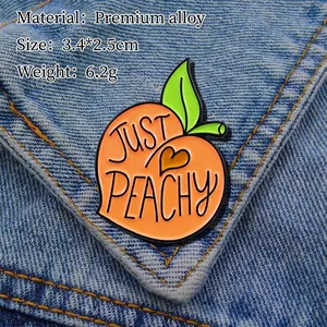 Just Peachy fruit enamel pin in orange and green on blue denim fabric background