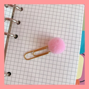 Pink fluffy pom pom gold metal paperclip bookmark on a minimalist grid notebook page