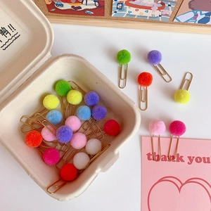 Close-up of golden paper clips with colorful fluffy pom poms for planners and bookmarks