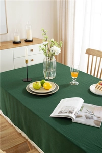 Detailed texture of dark green cotton tablecloth with elegant tassel trim in a home setting
