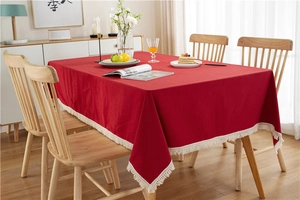 Detail of red cotton tablecloth with white decorative fringes on a wooden dining table