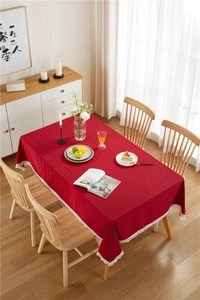 Detail of red cotton linen tablecloth with white tassel fringe on wooden dining table