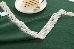 Close-up of deep green cotton tablecloth fabric featuring white tassel fringe detail