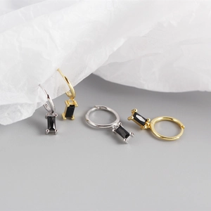 Macro detail of gold and silver rectangular black zircon earrings on white artistic paper